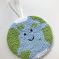 A hand-punched cotton yarn wall hanging depicting a smiling Earth with blue oceans and green landmasses, backed with felt and equipped with a ribbon for hanging.